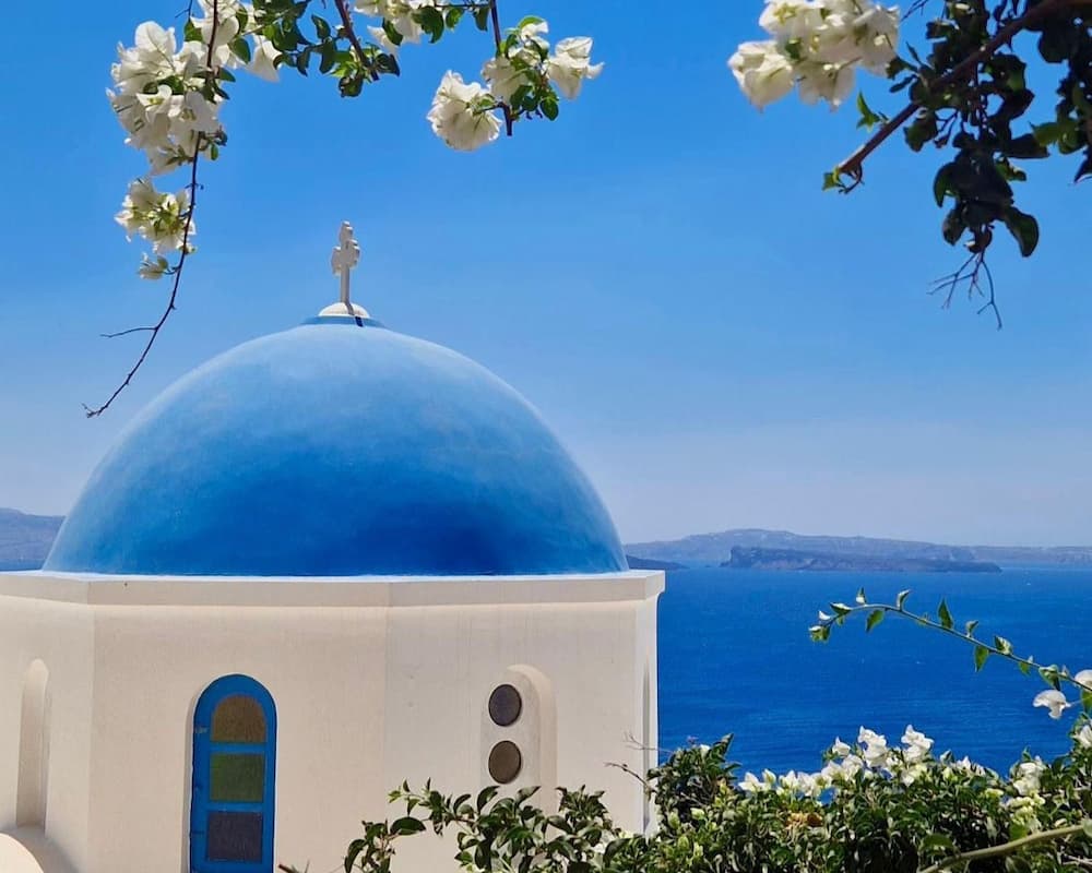 Santorini blauwe koepel witte bloemen en uitzicht op zee